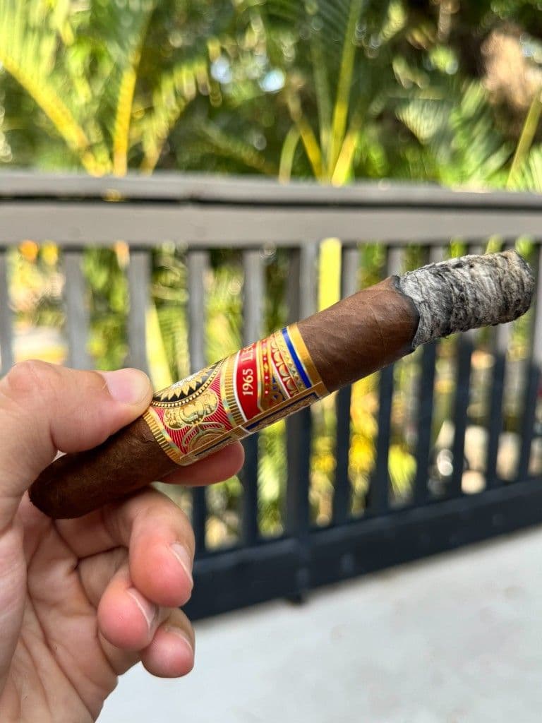 Perdomo Legacy mid-smoke with long even ash on a deck railing