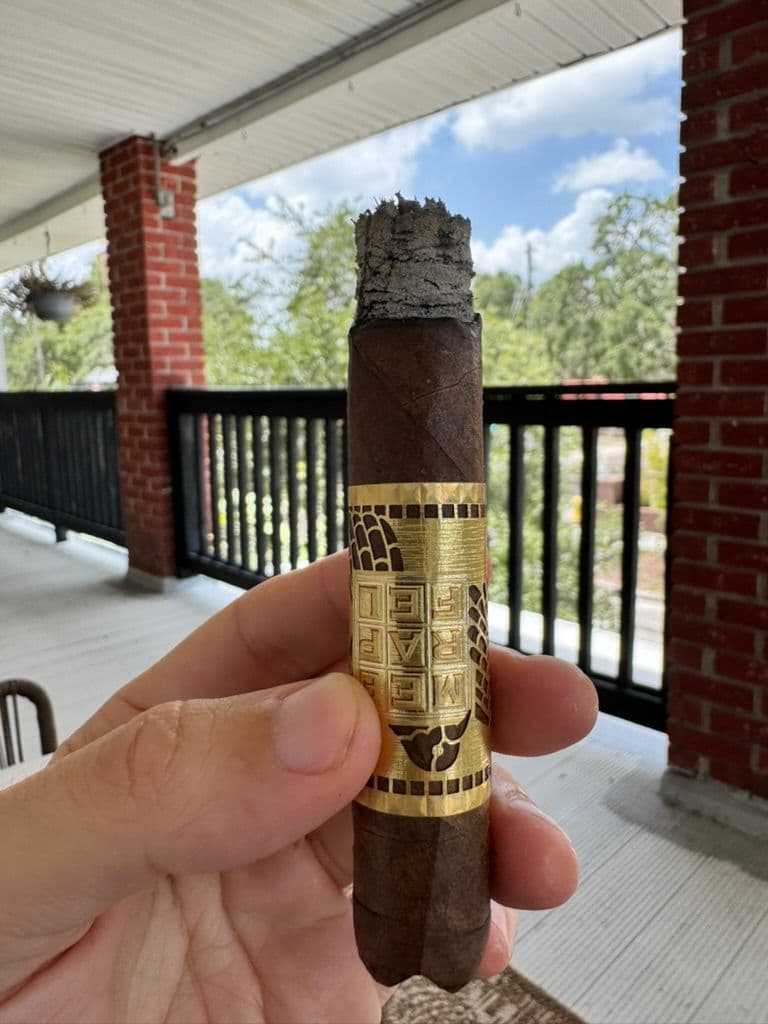 Création Liberté mid-smoke with ash and gold band on a balcony